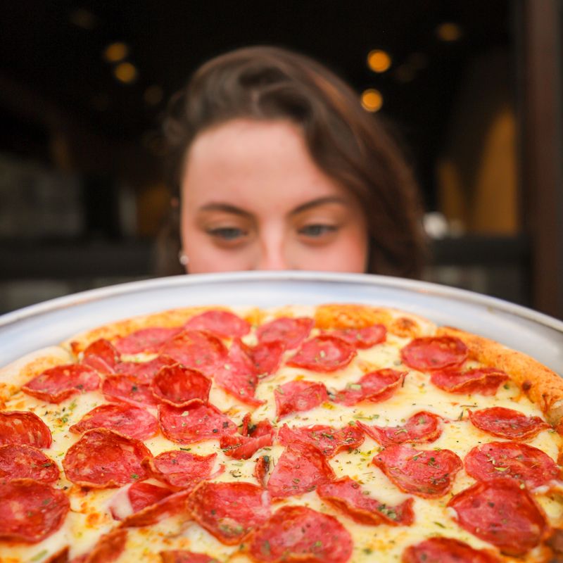 Mulher olha por cima de uma pizza de calabresa inteira na bandeja