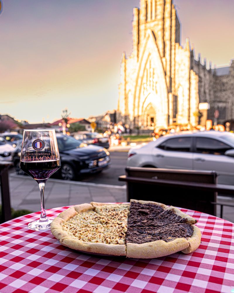 Pizza metade chocolate branco e metade chocolate preto com uma taça de vinho tinto, e a Catedral de Pedra ao fundo