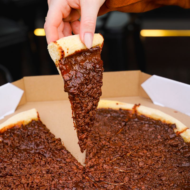 Mão tira uma fatia da pizza de chocolate preto da caixa