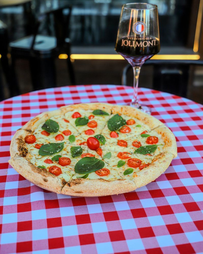 Pizza margherita com tomate cereja e manjericão na toalha xadrez, ao lado de uma taça de vinho tinto