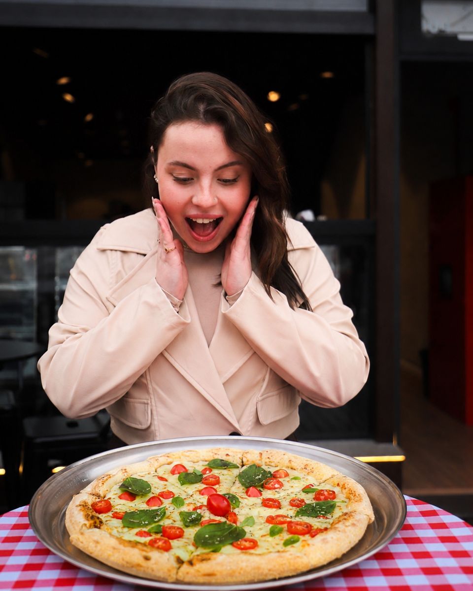Mulher surpresa diante de uma pizza grande de margherita na bandeja