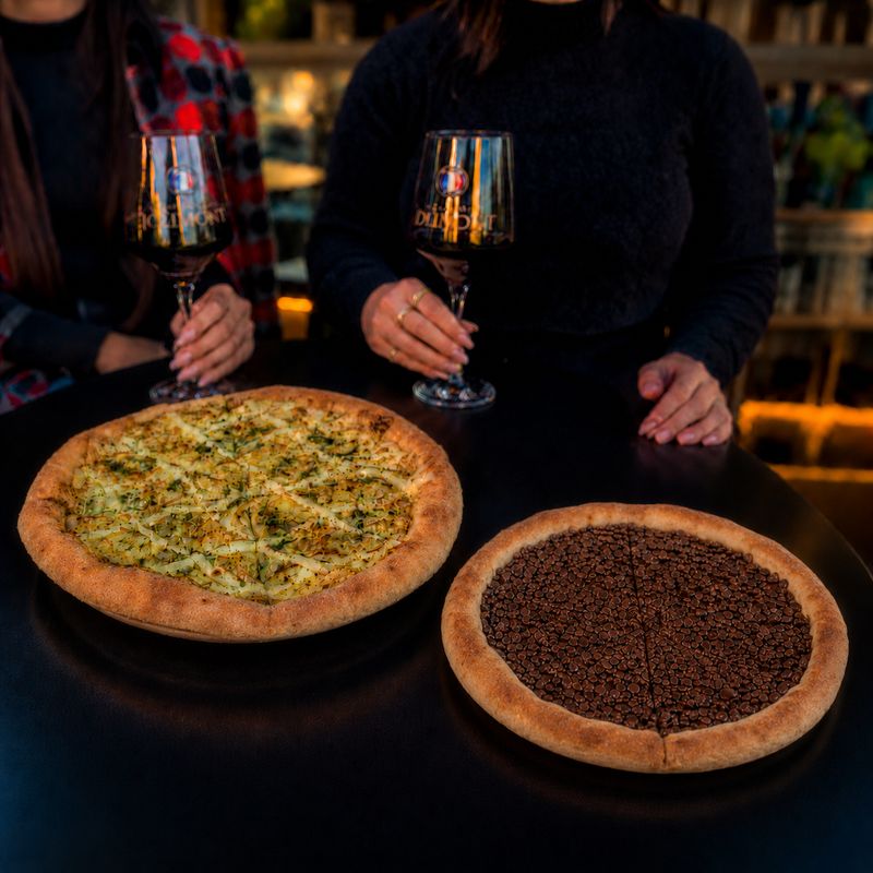 Pizza quatro queijos e pizza de chocolate na mesa, com duas taças de vinho tinto